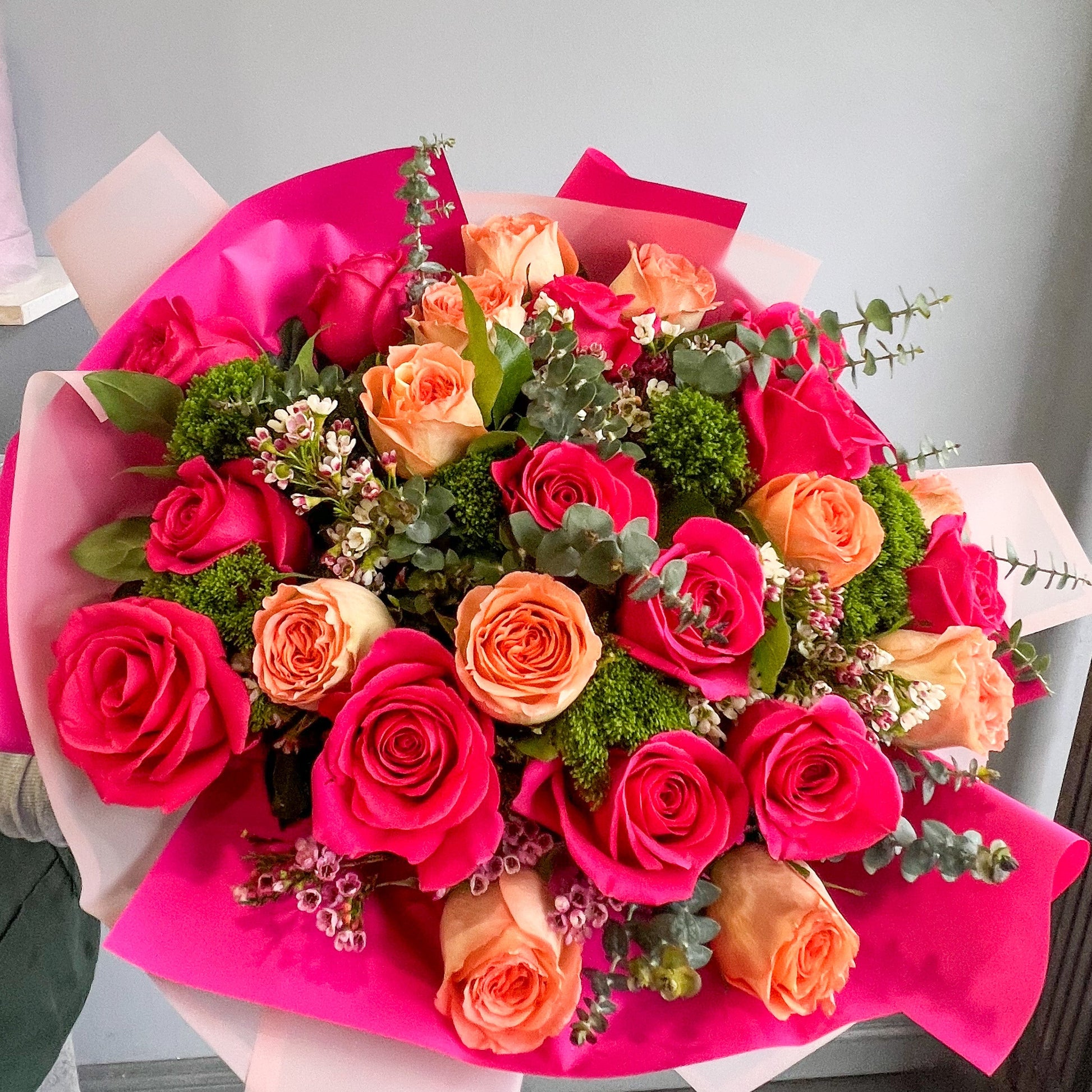 A stunning arrangement of hot pink and orange roses with lush green filler, creating a lively floral display.