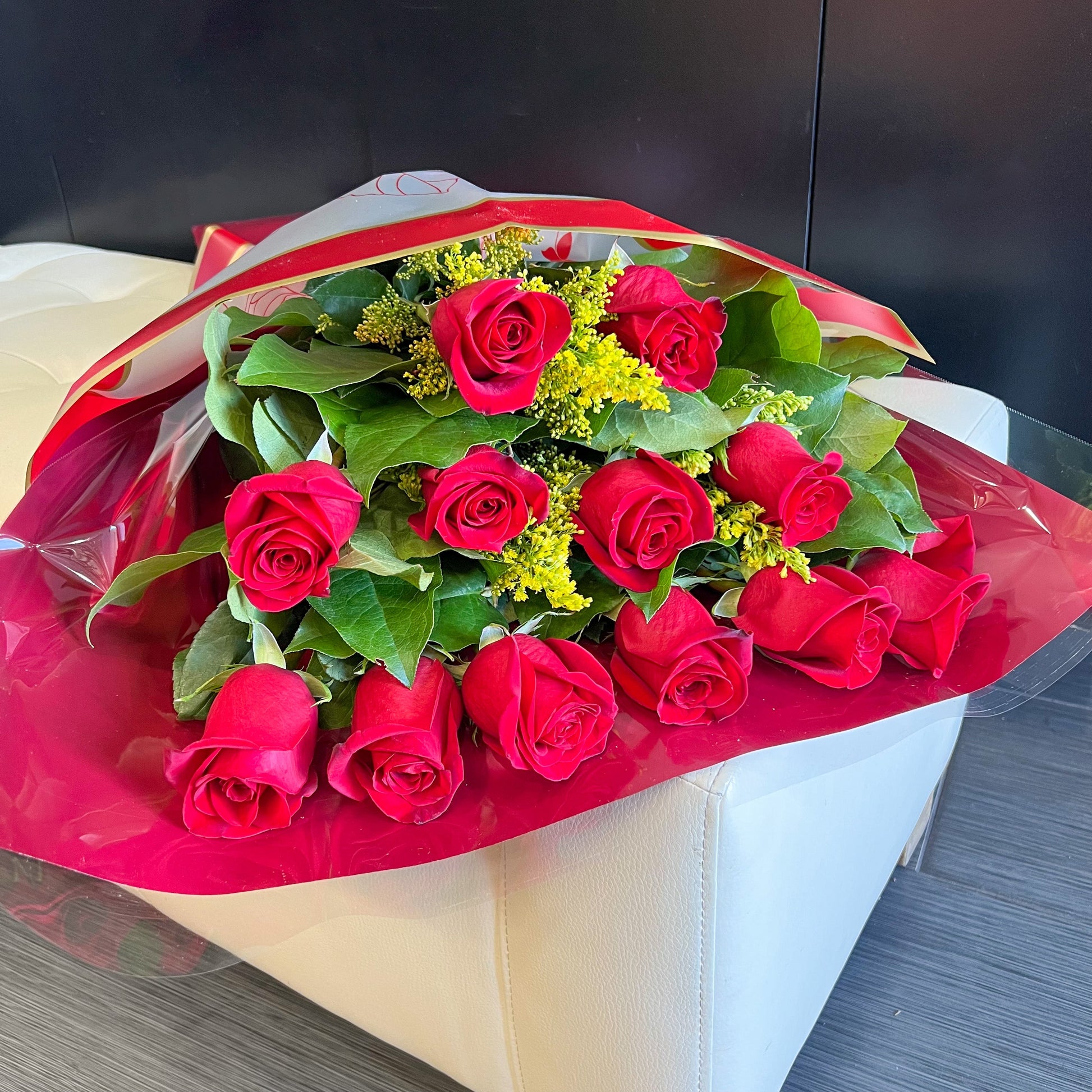 A wrapped bouquet of red roses elegantly placed on a pristine white couch, showcasing vibrant colors