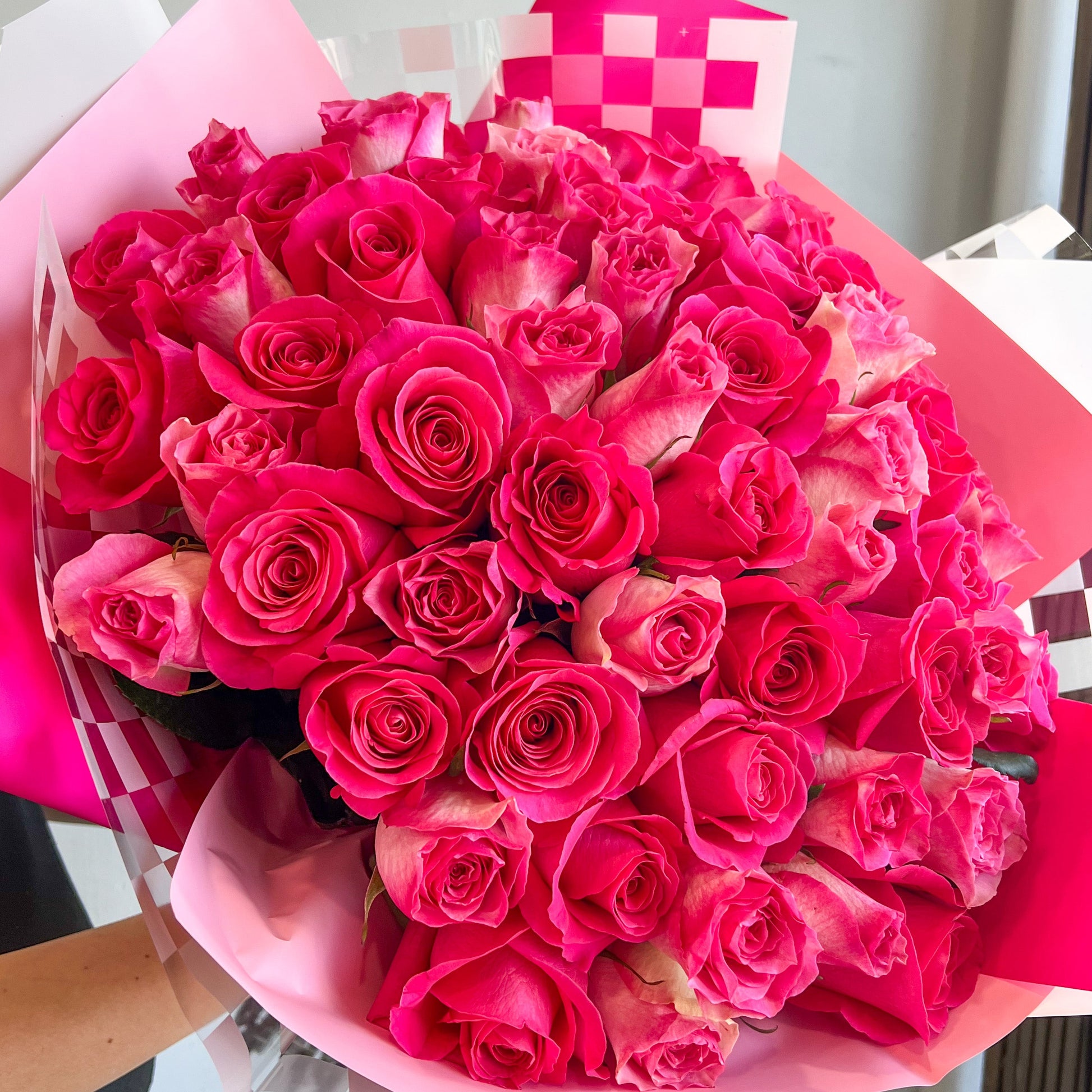A woman holds a vibrant bouquet of pink roses, showcasing their delicate petals and lush greenery.