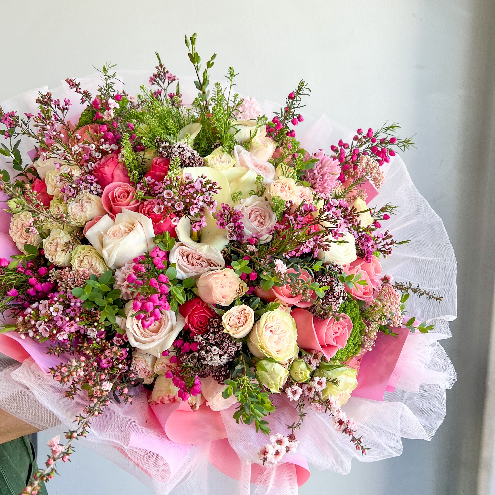 A woman holds a bouquet of pink and white flowers, featuring delicate pink tulle accents.