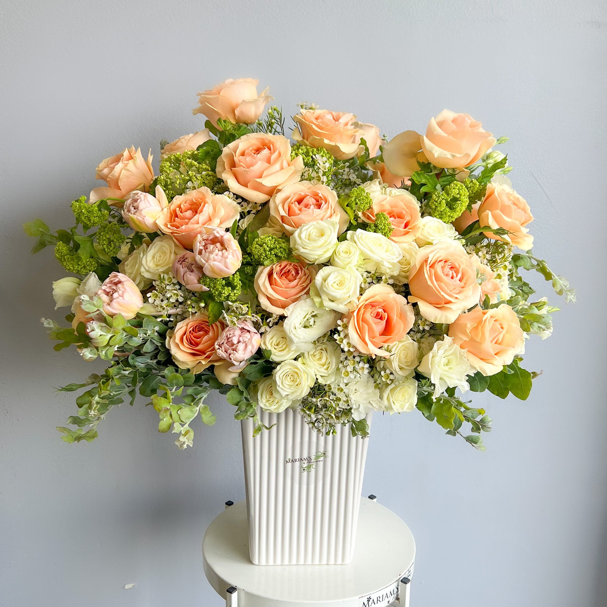 A large white vase brimming with bright orange roses, named 'Petal Pop', highlighting a beautiful floral display.