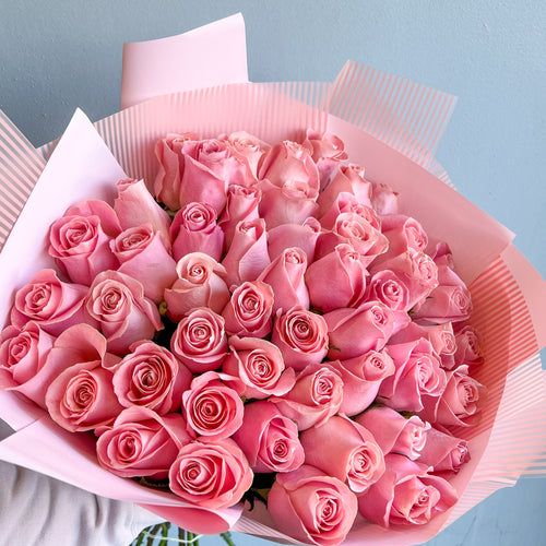 A hand holds a wrapped bouquet of 50 pink roses, showcasing their vibrant color and elegance without any filler