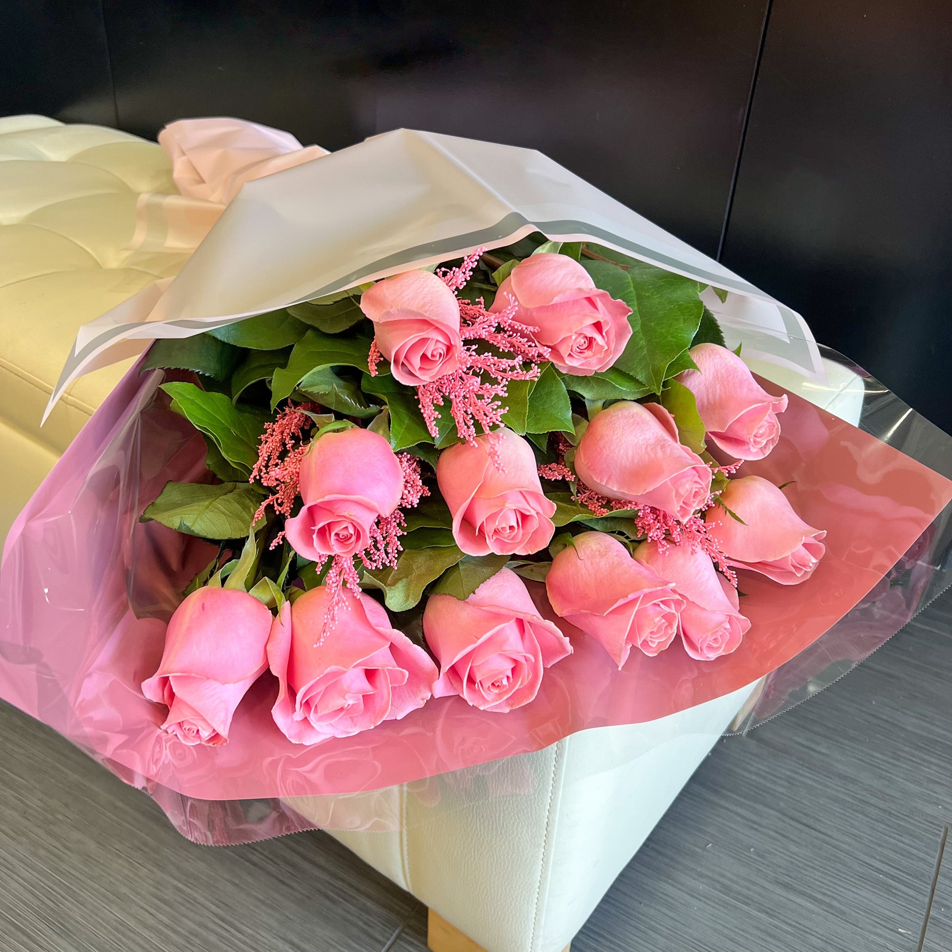 A wrapped bouquet of pink roses placed on a white couch, creating a soft and inviting atmosphere.