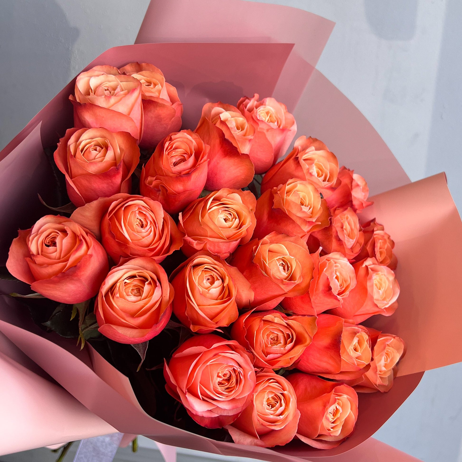 A vibrant bouquet of orange roses in a pink paper bag, highlighting the exquisite Kahala Roses without any fillers