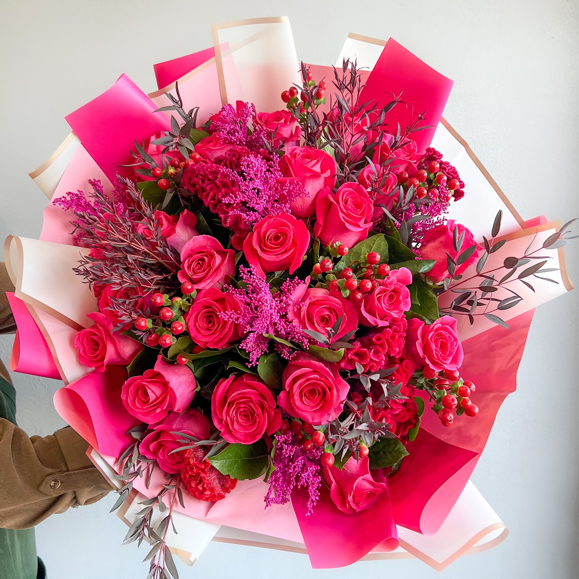 A woman elegantly holds a wrapped bouquet of vibrant hot pink roses, showcasing their beauty and freshness