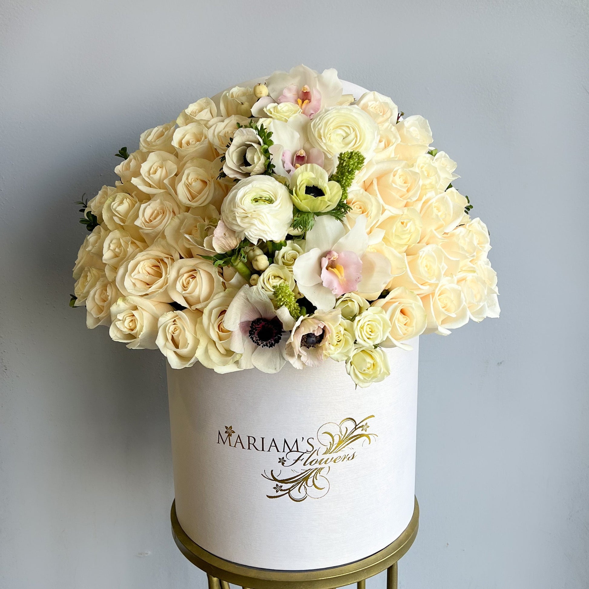 A white box adorned with seasonal flowers, including white roses, placed elegantly on a table.