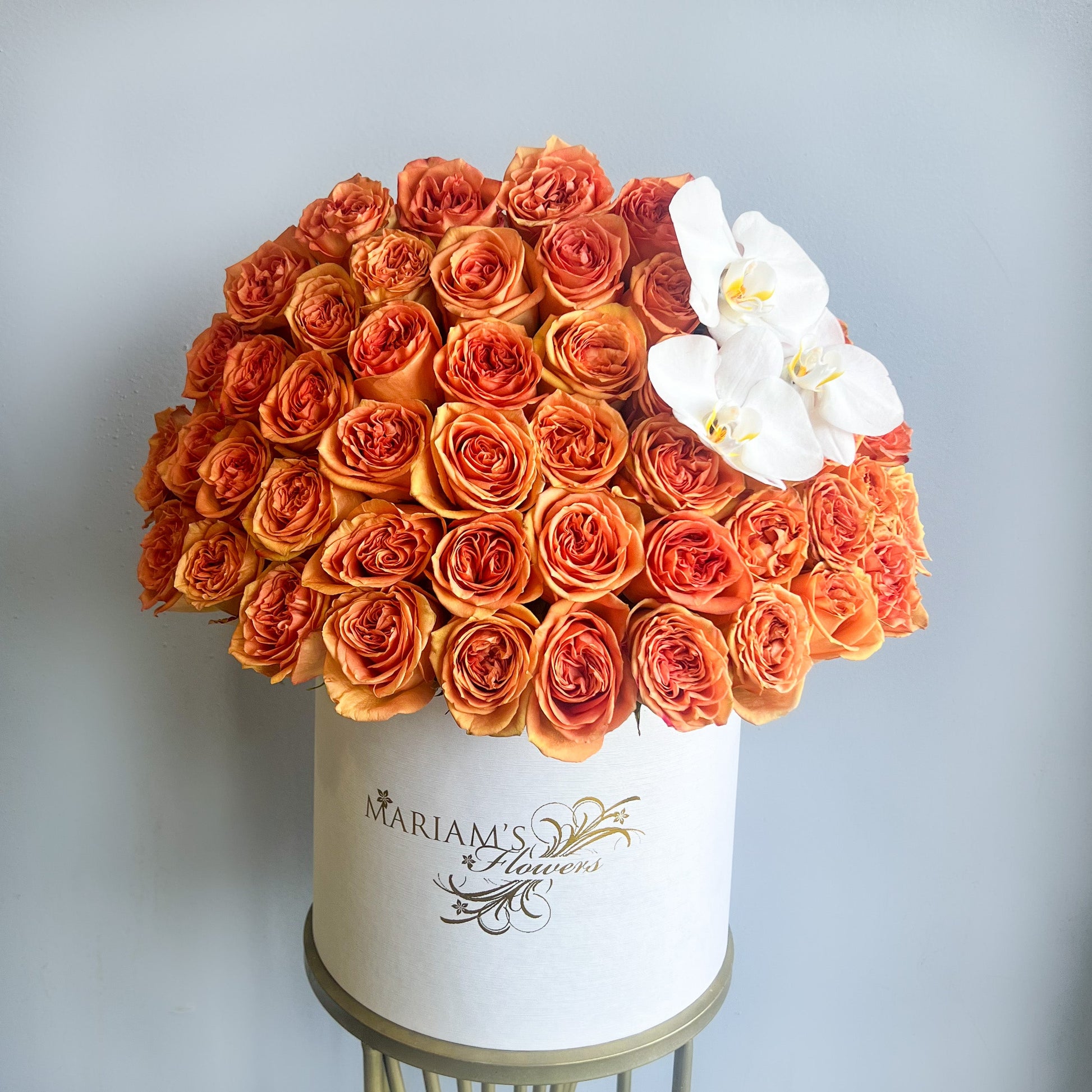 A charming floral display featuring orange roses and a white orchid in a pristine white box, ideal for gifting or decor