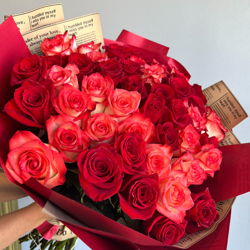 A stunning arrangement of 50 red and blush roses, wrapped beautifully, with a newspaper nestled in the middle