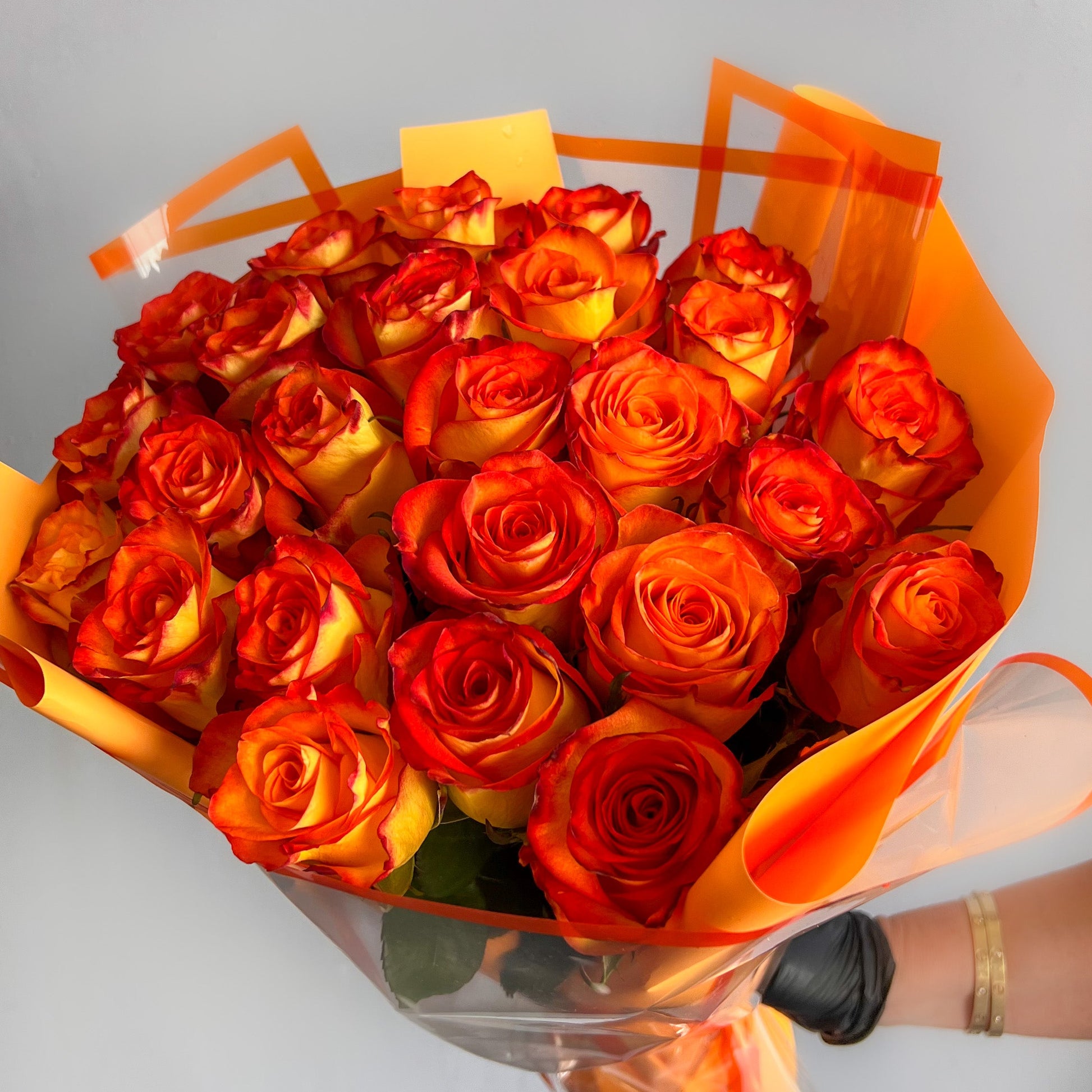 A bouquet of bright orange roses held in a hand, wrapped elegantly, representing the charm of High Magic Roses