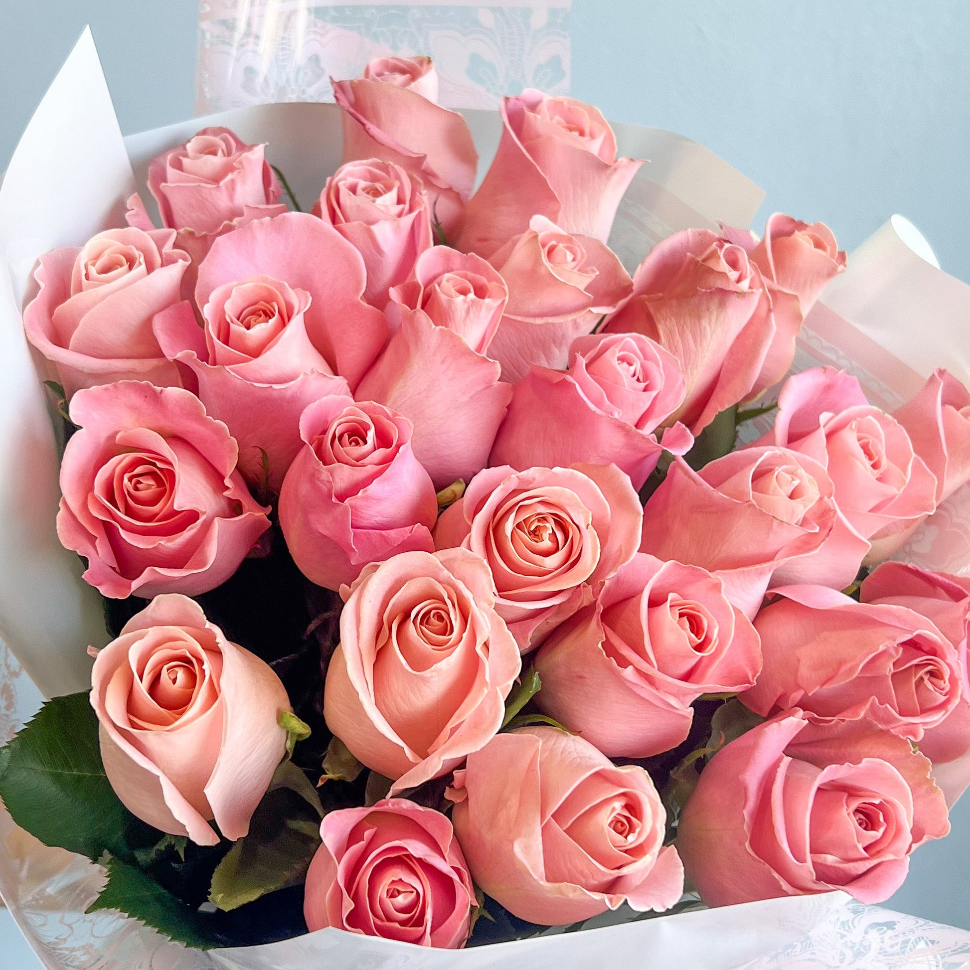 A wrapped bouquet of pink roses in white paper, elegantly presented with no additional filler flowers