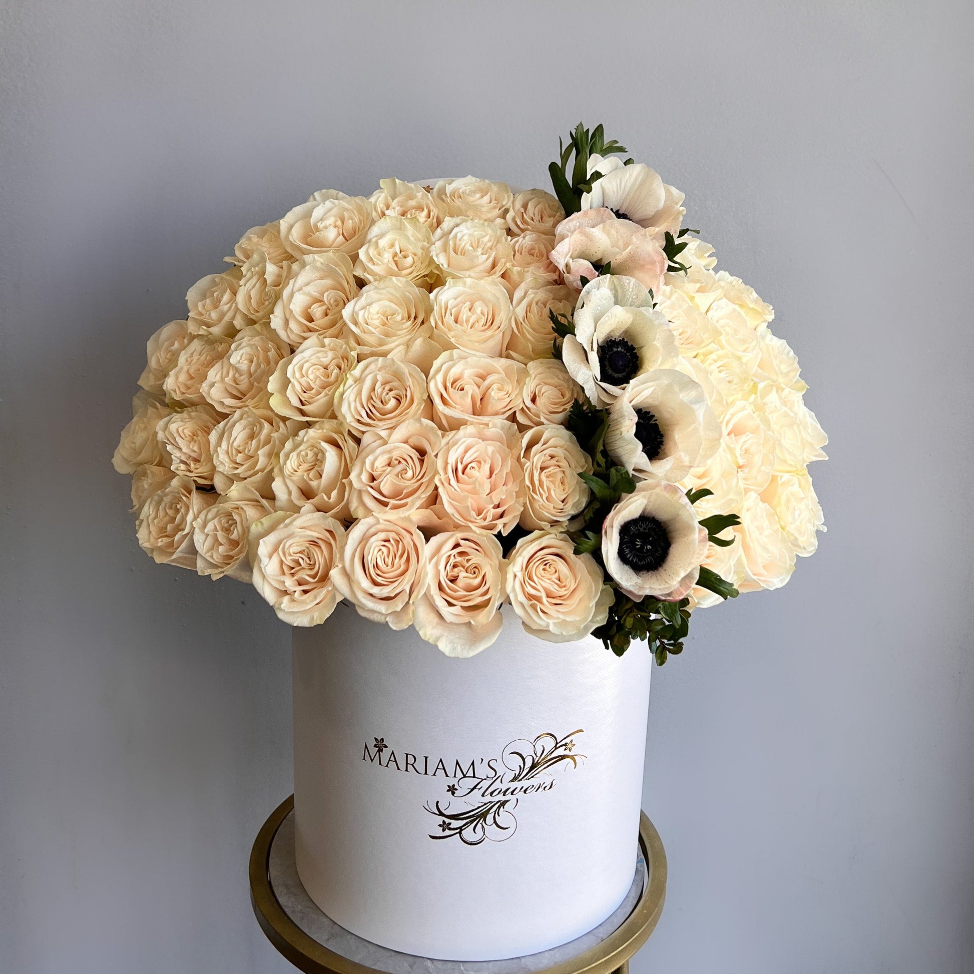 A white box filled with white roses and colorful anemones, showcasing a floral arrangement.