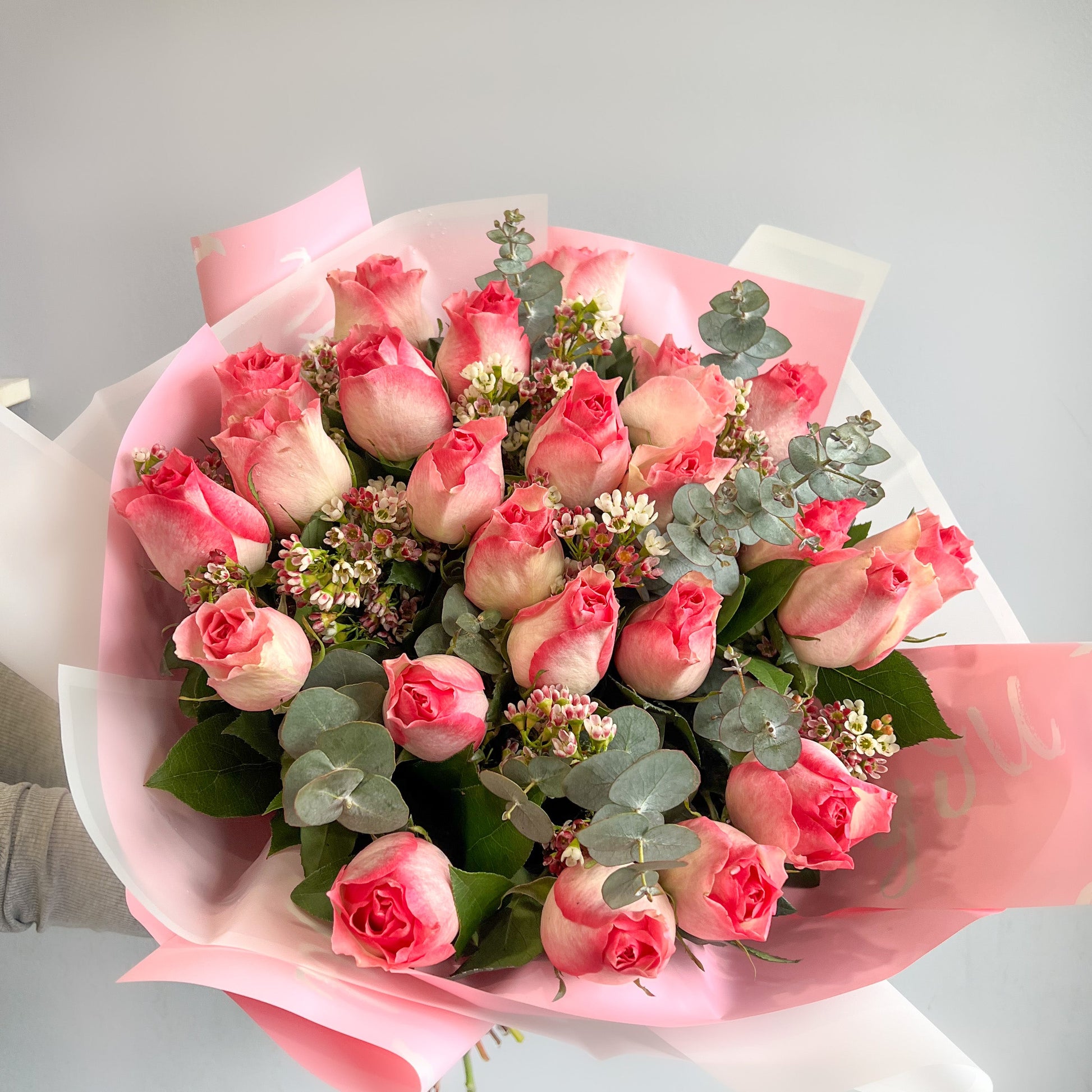 A hand displays a bouquet of pink Malibu roses, accented with filler flowers.