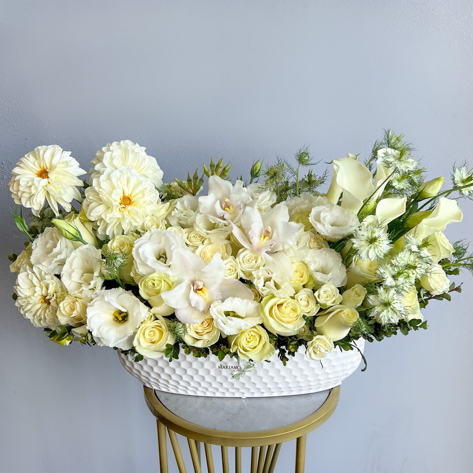 A white floral arrangement featuring various white flowers elegantly displayed on a pedestal vase.