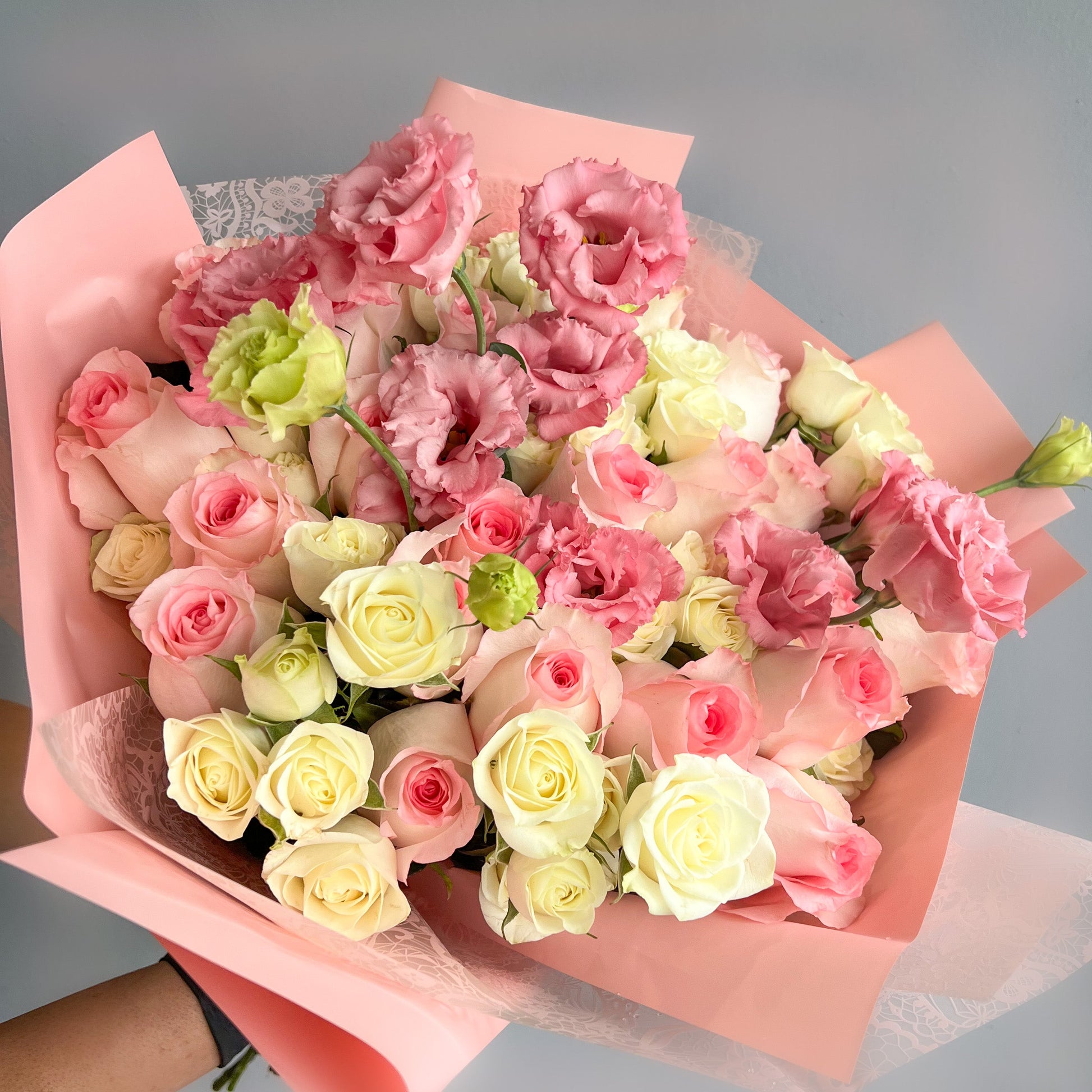 A hand holding Mariam's Signature Bouquet featuring pink and white roses elegantly wrapped together