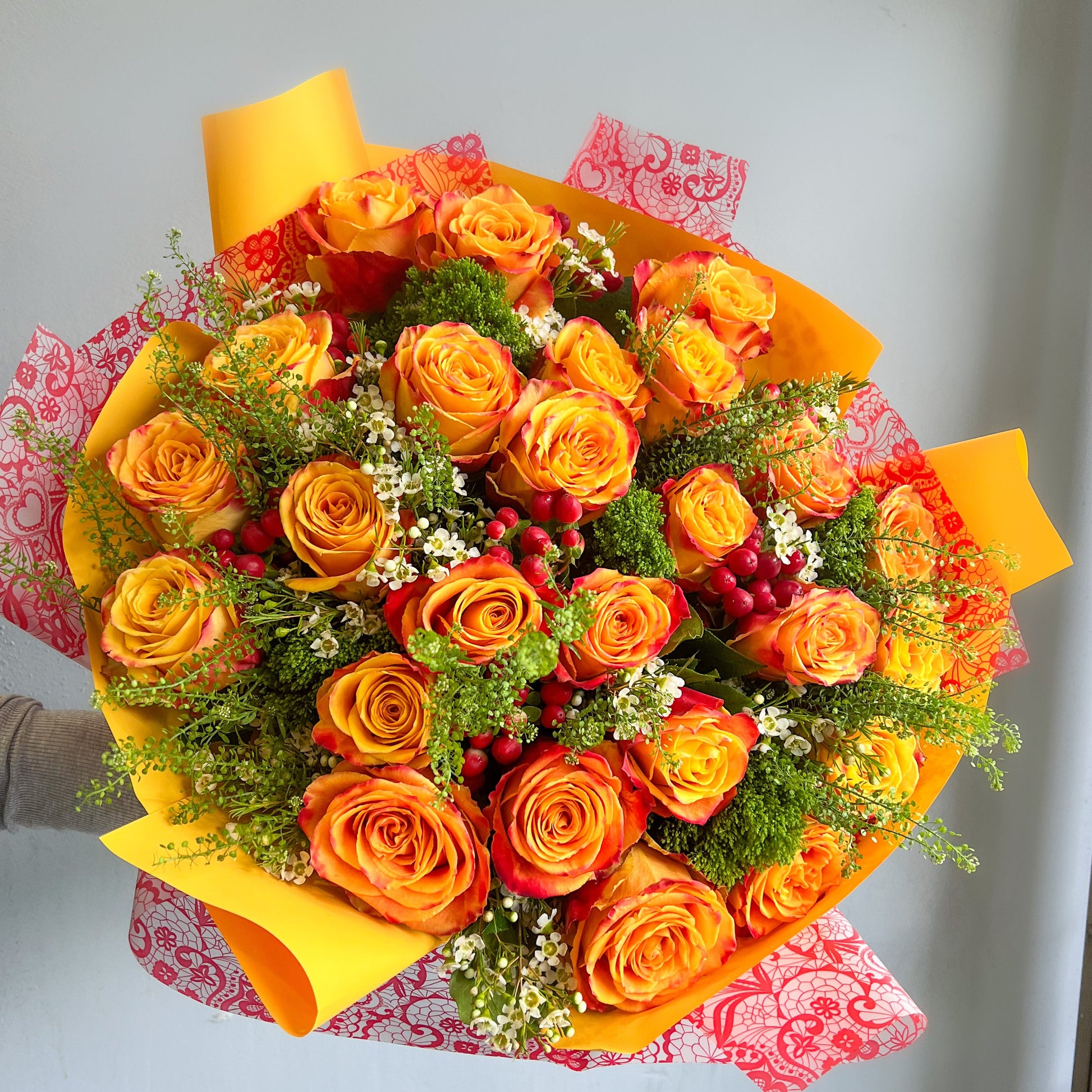 A bouquet featuring vibrant orange and yellow roses, complemented by delicate filler flowers.