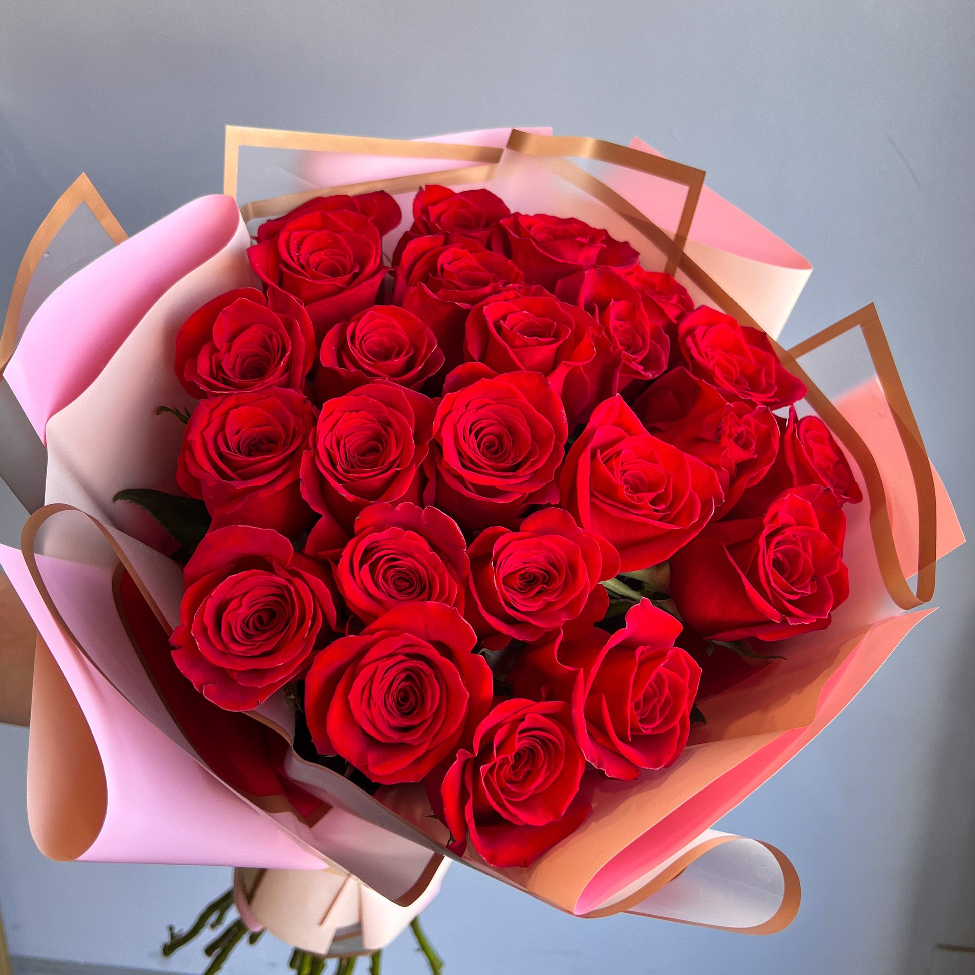 A bouquet of 25 red roses, elegantly arranged in a paper box, showcasing their vibrant beauty without any filler